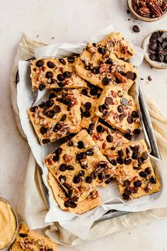 chocolate chip cookie bars on parchment paper next to bowls of nuts