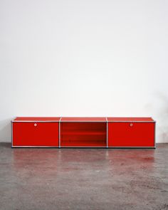 a red cabinet sitting on top of a cement floor next to a white wall in an empty room