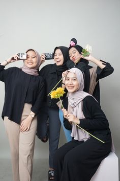 four women posing for a photo with flowers in their hair and one holding a camera