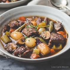 a white bowl filled with beef stew and carrots on top of a marble table