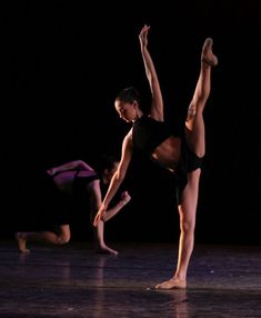 two dancers in black leotards and one is doing a handstand on the floor