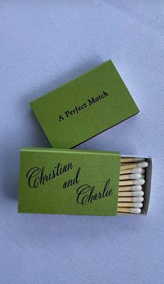 two matches are sitting in a match box on a blue surface, one is green and the other is white