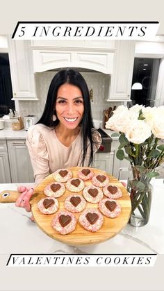 a woman holding a wooden platter with heart shaped cookies on it and flowers in the background