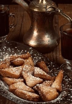 powdered sugar cookies on a plate next to a cup of tea and a kettle