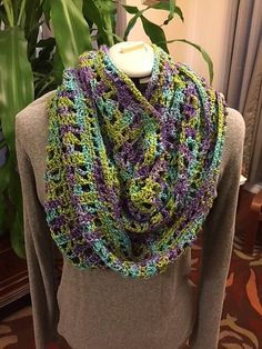 a woman wearing a purple and green crocheted scarf on top of a mannequin