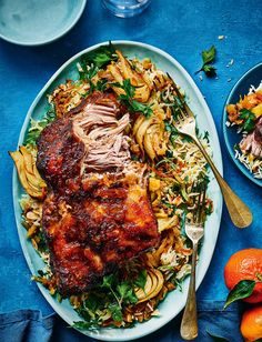 a plate with meat and pasta on it next to some oranges, silverware