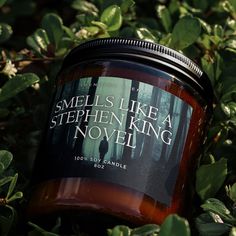 a candle sitting in the middle of some leaves and bushes with words on it that read smells like a stephen king novel