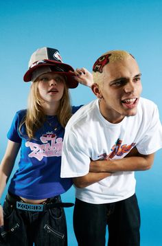 two people standing next to each other in front of a blue background with one person wearing a hat