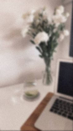 an open laptop computer sitting on top of a white table next to a vase with flowers