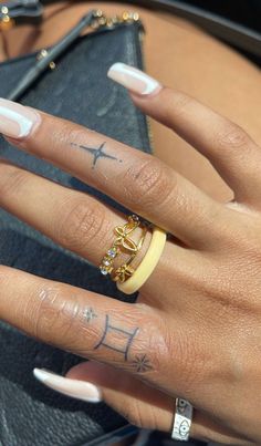 a woman's hand with two rings on it and a cross tattooed on the middle finger