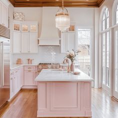 a kitchen with pink cabinets and white counter tops, an island in the middle is surrounded by glass doors