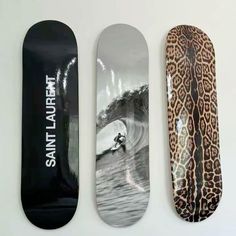 three skateboards with different designs on them are lined up against a white wall, one is black and the other is leopard print