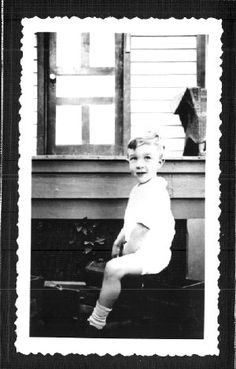 an old photo of a young boy sitting on top of a suitcase in front of a window