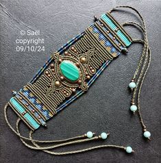 a beaded necklace with turquoise and gold beads on a black surface, next to an earring