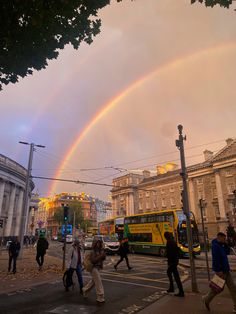 people crossing the street with a rainbow in the sky above them and buildings on either side