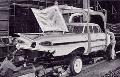 two men working on an old car being worked on by another man in the background