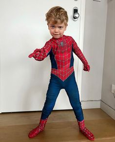 a young boy dressed in a spiderman costume standing on the floor next to a door