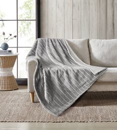 a couch with a blanket on it in front of a wooden wall and floor next to a window