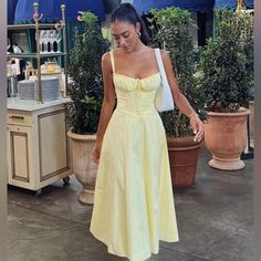 a woman in a yellow dress is standing near potted plants and looking down at the ground