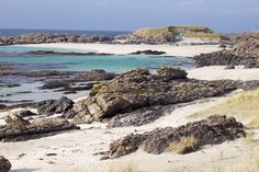 a sandy beach next to the ocean with lots of rocks and grass on top of it