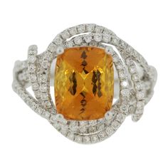 A brilliant ring featuring a GIA certified natural yellowish-orange sapphire! It weighs 4.84 carats and is free of any eye-visible inclusions allowing the stones natural brilliance and bright color to shine! It is shaped as a cushion and is accented by 1.18 carats of round brilliant-cut diamonds set in 18k white gold swirls around the ring and sapphire. Made in 18k white gold and ready to be worn! Ring Size 6 Fine Jewelry Orange Sapphire Anniversary Ring, Orange Sapphire Ring For Anniversary, Orange Diamond Topaz Ring With Center Stone, Orange Diamond Ring With Prong Setting, Orange Diamond Rings With Prong Setting, Orange Topaz Ring With Diamond Center Stone, Orange Topaz Ring With Prong Setting, Orange Diamond Gemstone Ring, Orange Diamond Rings With Gemstone