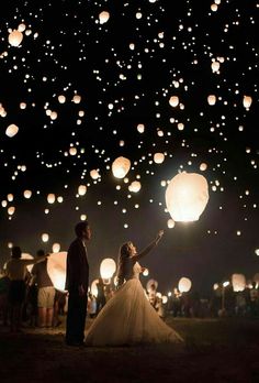 a bride and groom holding hands in front of lanterns floating in the air at night