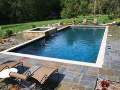 an empty swimming pool surrounded by lawn chairs and landscaping equipment in the background, with a stone patio around it