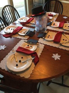 the table is set with plates and napkins for snowman themed holiday dinnerware