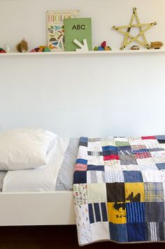 a bed with a quilt on top of it next to a wall mounted book shelf