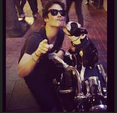 a man is sitting on a motorcycle with his dog in front of him and giving the peace sign