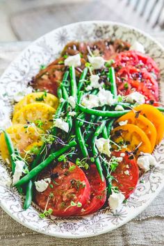 a white plate topped with green beans, tomatoes and feta cheese on top of it