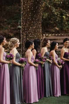 a group of women standing next to each other wearing purple and grey dresses with flowers in their hair