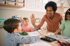 a woman sitting at a table with two children in front of her and holding their hands up