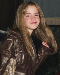 a young woman with long hair wearing a brown leather jacket and smiling at the camera