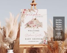 an easel with a welcome sign in front of some pampokin flowers and feathers