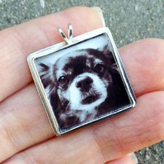 a hand holding a small square pendant with a black and white dog photo on it