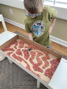 a young boy standing in front of a cardboard box filled with hot dogs on the floor