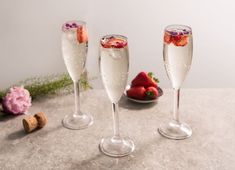 three champagne flutes with strawberries in them on a table next to flowers and wine corks