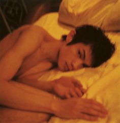 a shirtless man laying on top of a bed next to a white pillow and blanket