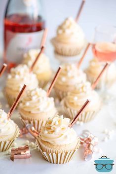 cupcakes with white frosting and rose gold decoration on top are lined up next to glasses