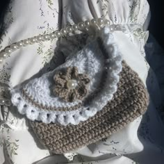 a crocheted purse sitting on top of a white pillow next to a beaded necklace