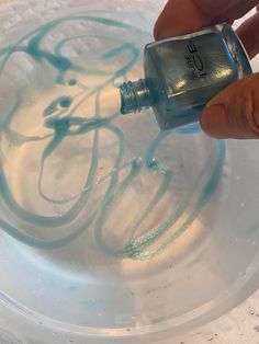 a hand holding a nail polish bottle in front of a white plate with blue swirls on it