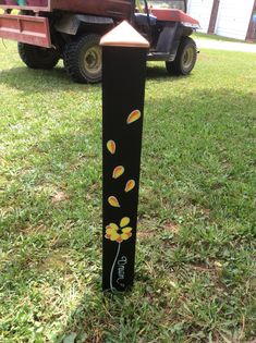 a black pole with yellow flowers painted on it in the grass next to a red truck