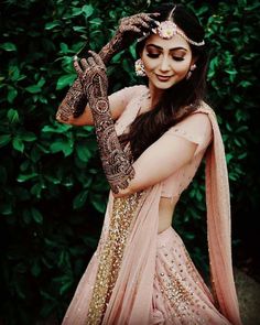 a woman in a pink lehenga holding her hands up to her face and looking at the camera