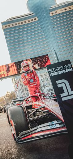 a man standing on top of a race car in front of tall buildings