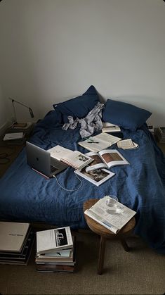 an unmade bed with many books on it and a laptop sitting on the end table