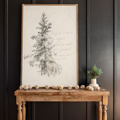 a wooden table sitting next to a wall with a framed tree on top of it