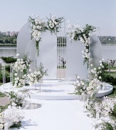 an outdoor ceremony setup with white flowers and greenery on the ground, surrounded by water