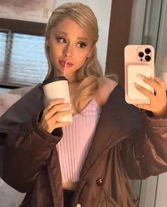 a woman taking a selfie with her cell phone and drinking from a coffee cup