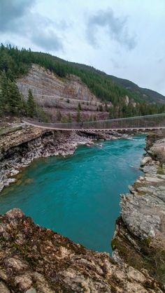 a suspension bridge over a river in the middle of a rocky area with trees on both sides